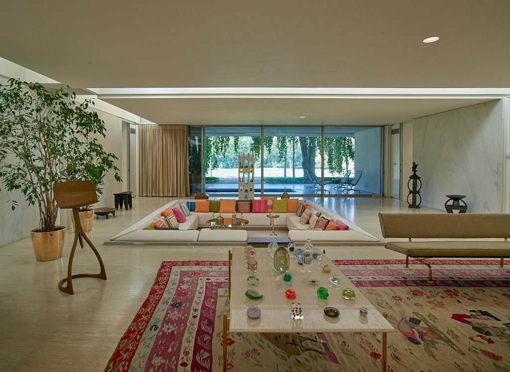 Floral rug beside pale flooring and a plain sofa at Miller House, with coloured cushions and garden-facing glass beyond.