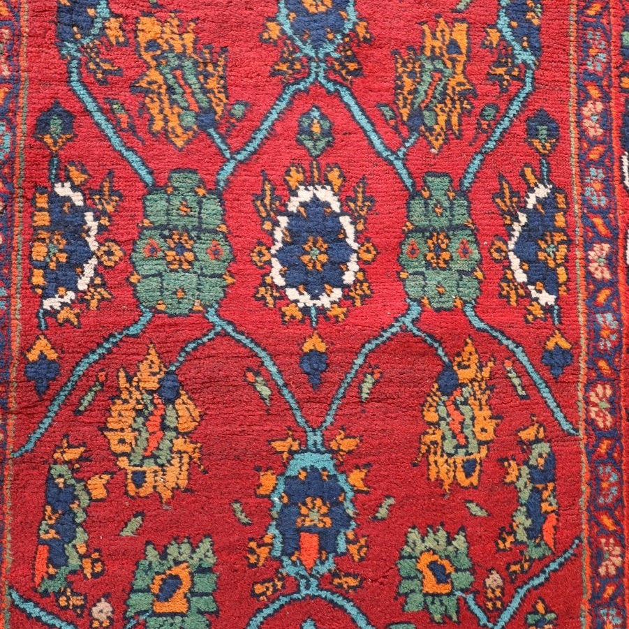 Mina Khani rug detail with blue and cream rosettes, green flowers and turquoise bands on red