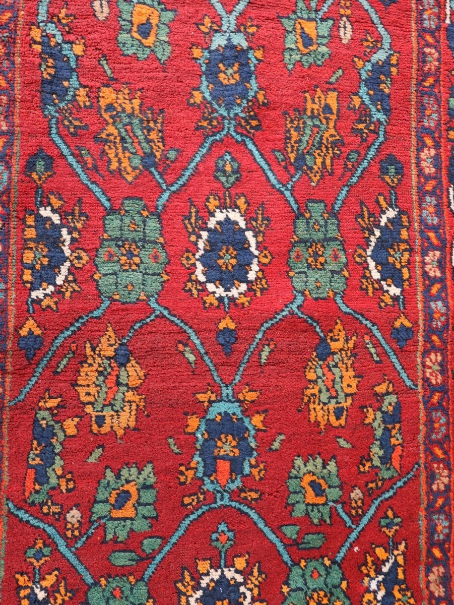 Mina Khani rug detail with blue and cream rosettes, green flowers and turquoise bands on red