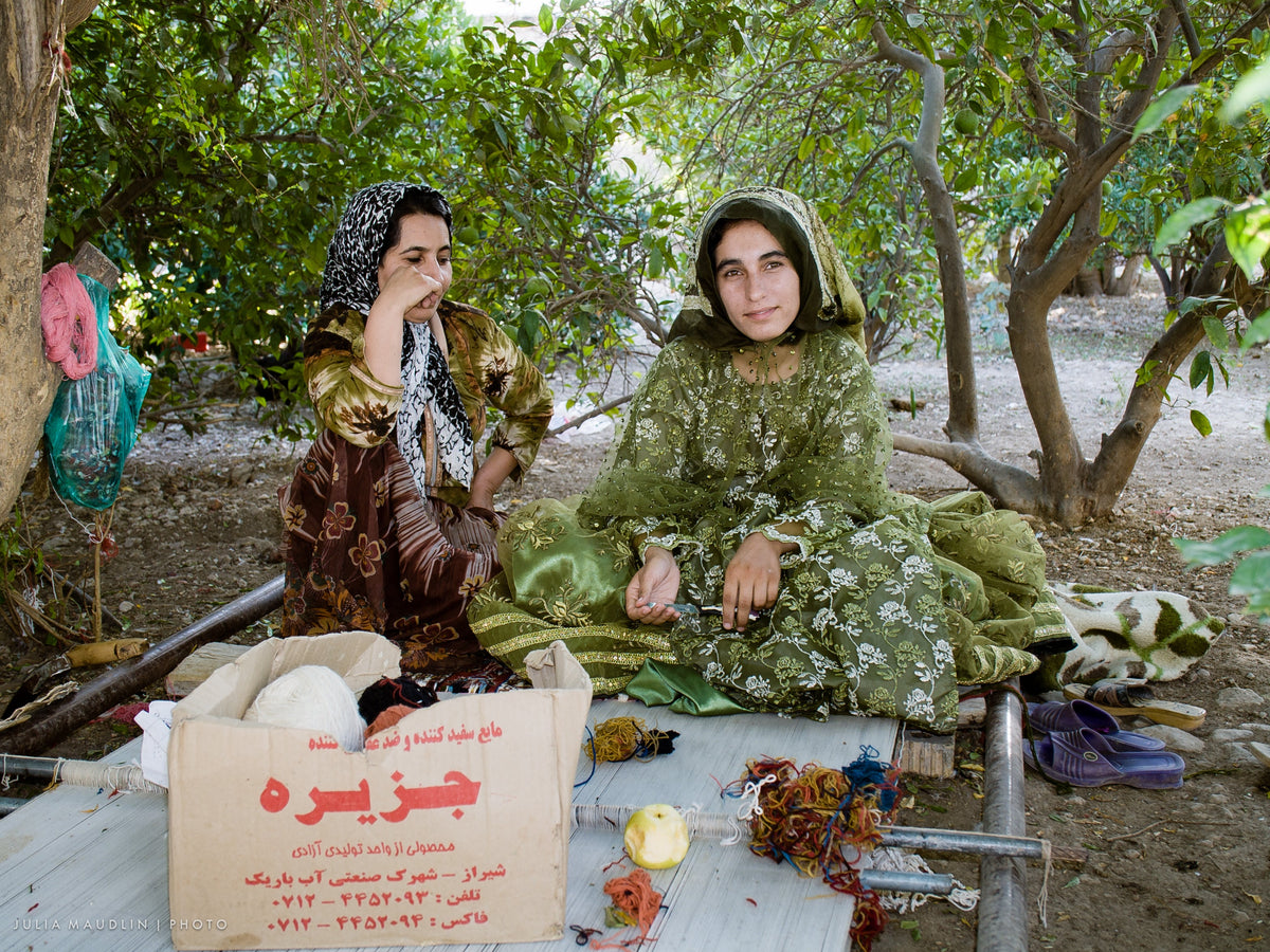 Two Qashqai weavers with coloured wool yarn beside a floor loom near Firuzabad, Iran