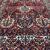 Angled view of Bakhtiari wool rug showing red and ivory floral design, patterned border and fringe.