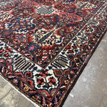 Diagonal view of Bakhtiari rug showing the ivory border, multicolored floral motifs and corner fringe.