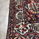 Close-up of Bakhtiari rug corner showing the ivory border, stylized tree motif and white fringe.
