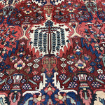 Detail of Bakhtiari rug field with an ivory tree motif surrounded by red, navy and green floral patterns.