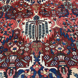 Detail of Bakhtiari rug field with an ivory tree motif surrounded by red, navy and green floral patterns.