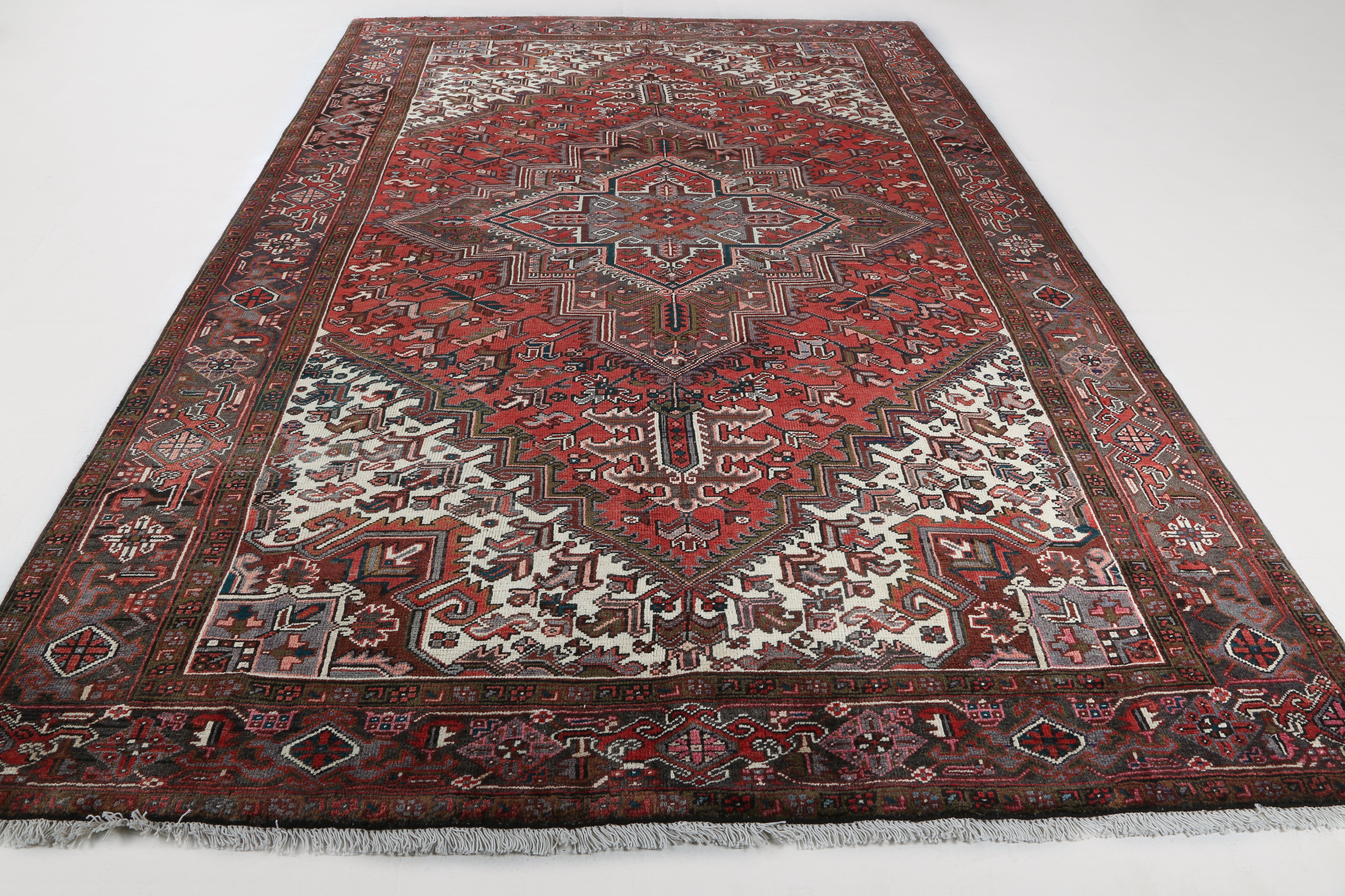 Persian Heriz rug with red medallion, cream panels, and dark border; fringed ends.