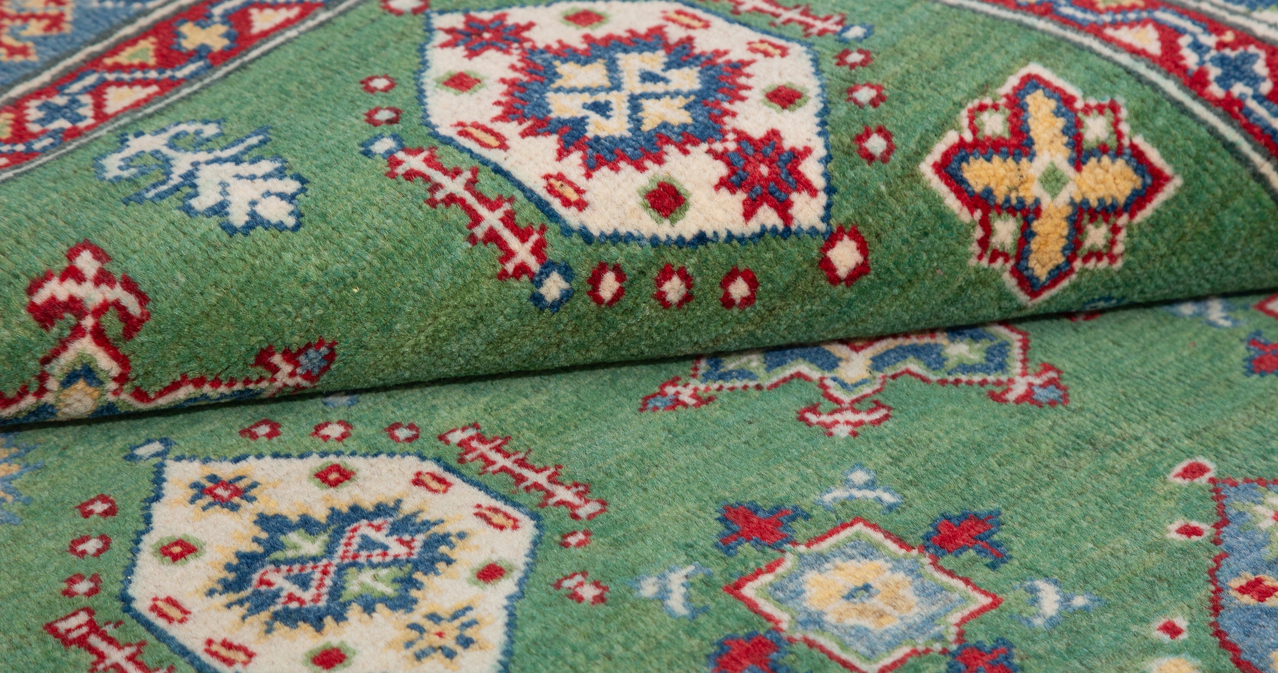 Folded edge and wool pile of green & red Kazak-inspired wool rug 29347.