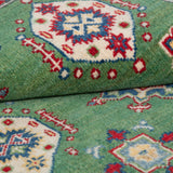 Folded edge and wool pile of green & red Kazak-inspired wool rug 29347.