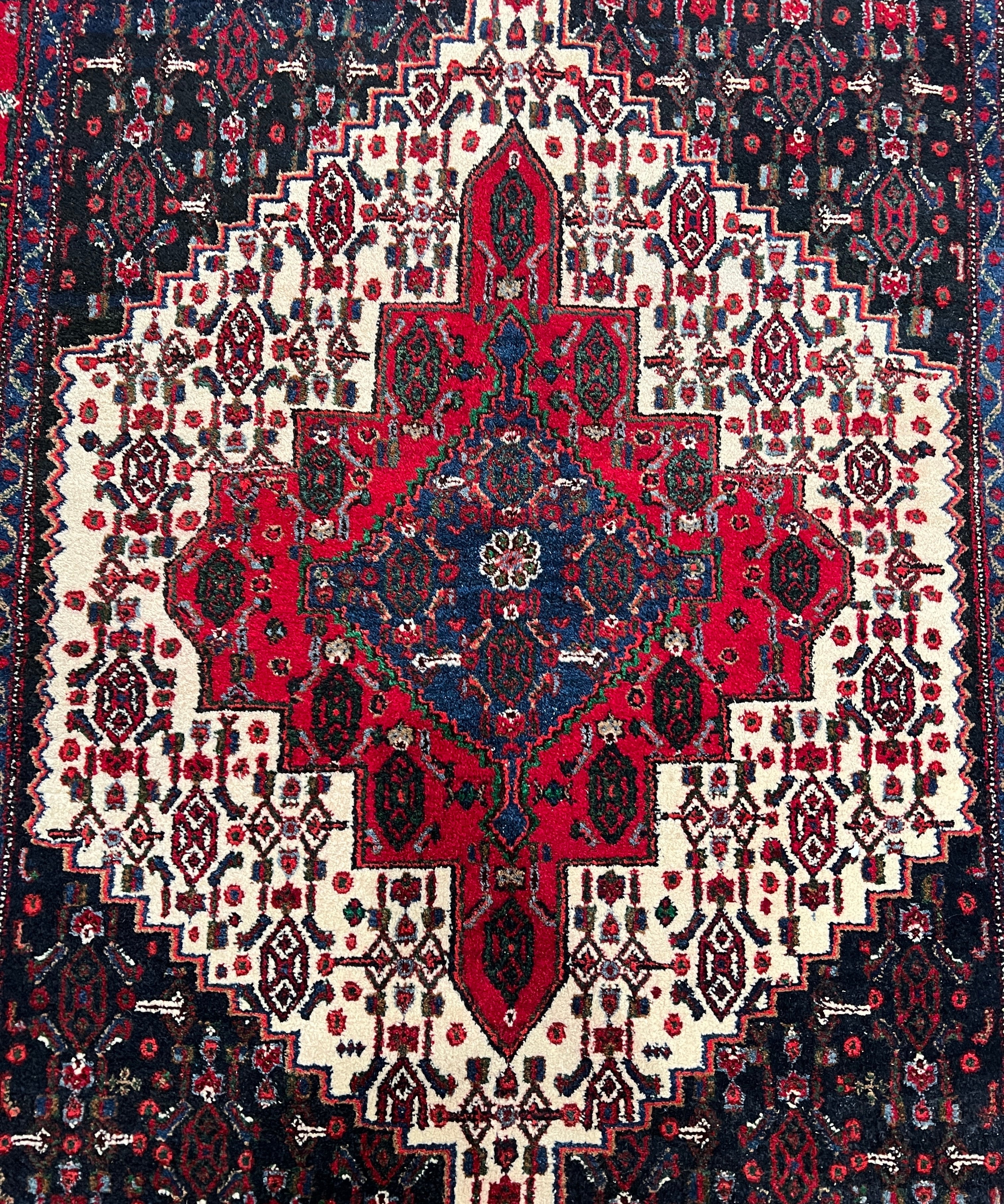 Persian Senneh rug with red center medallion, navy field, cream motifs