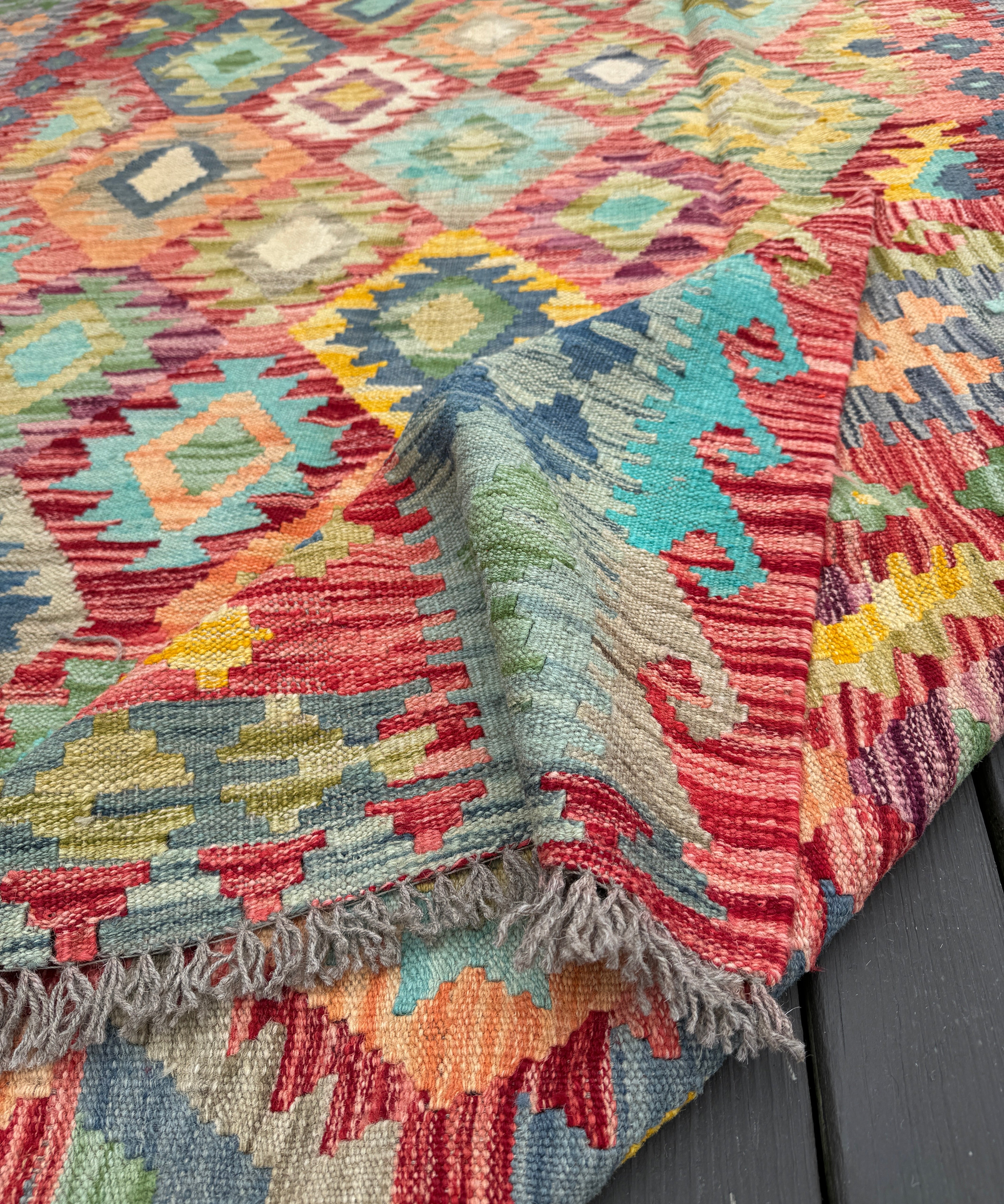 Colorful kilim rug with geometric pattern and fringed corner, close-up