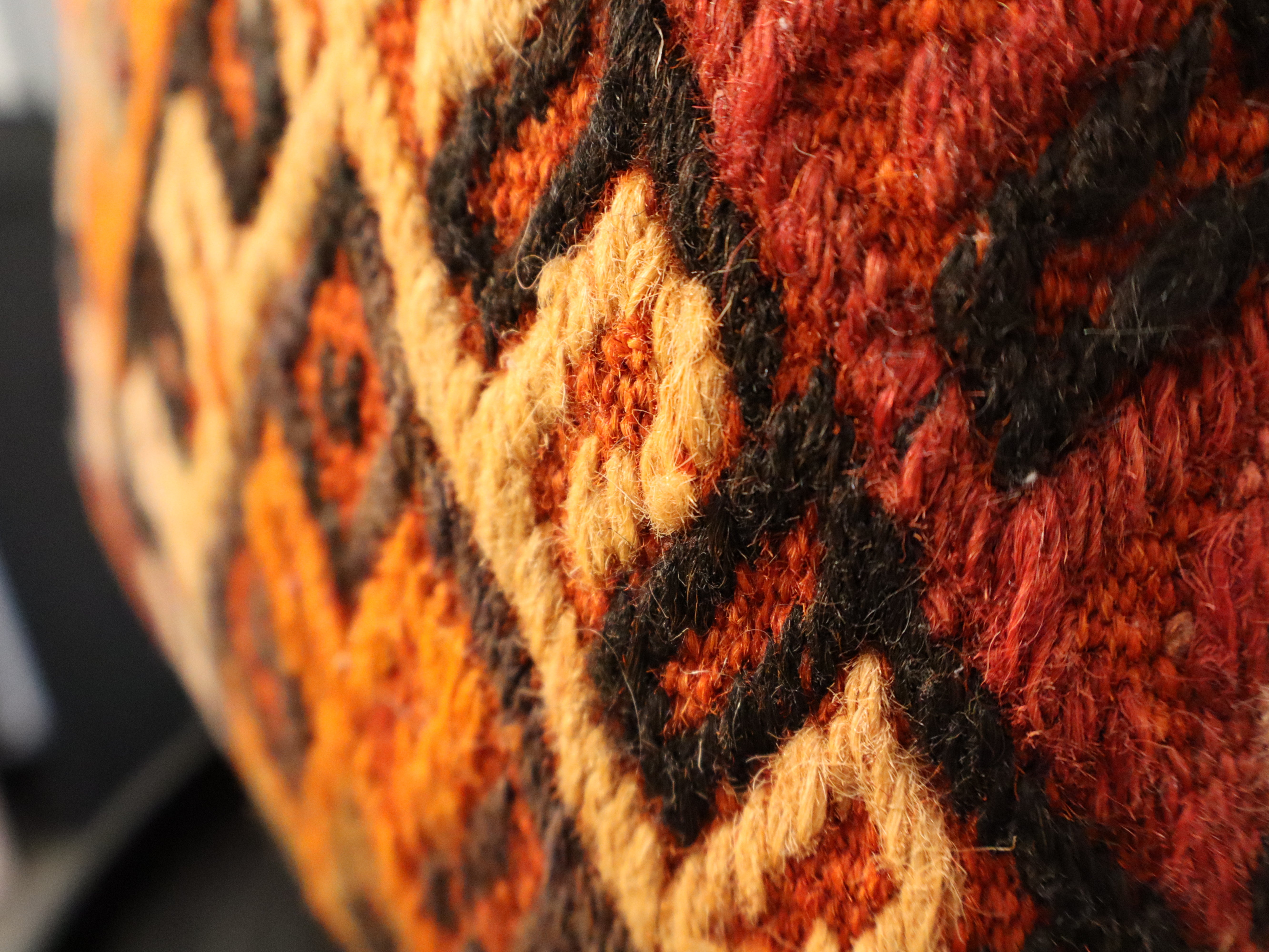 Close-up of woven geometric pillow fabric with orange, rust, black, and cream threads
