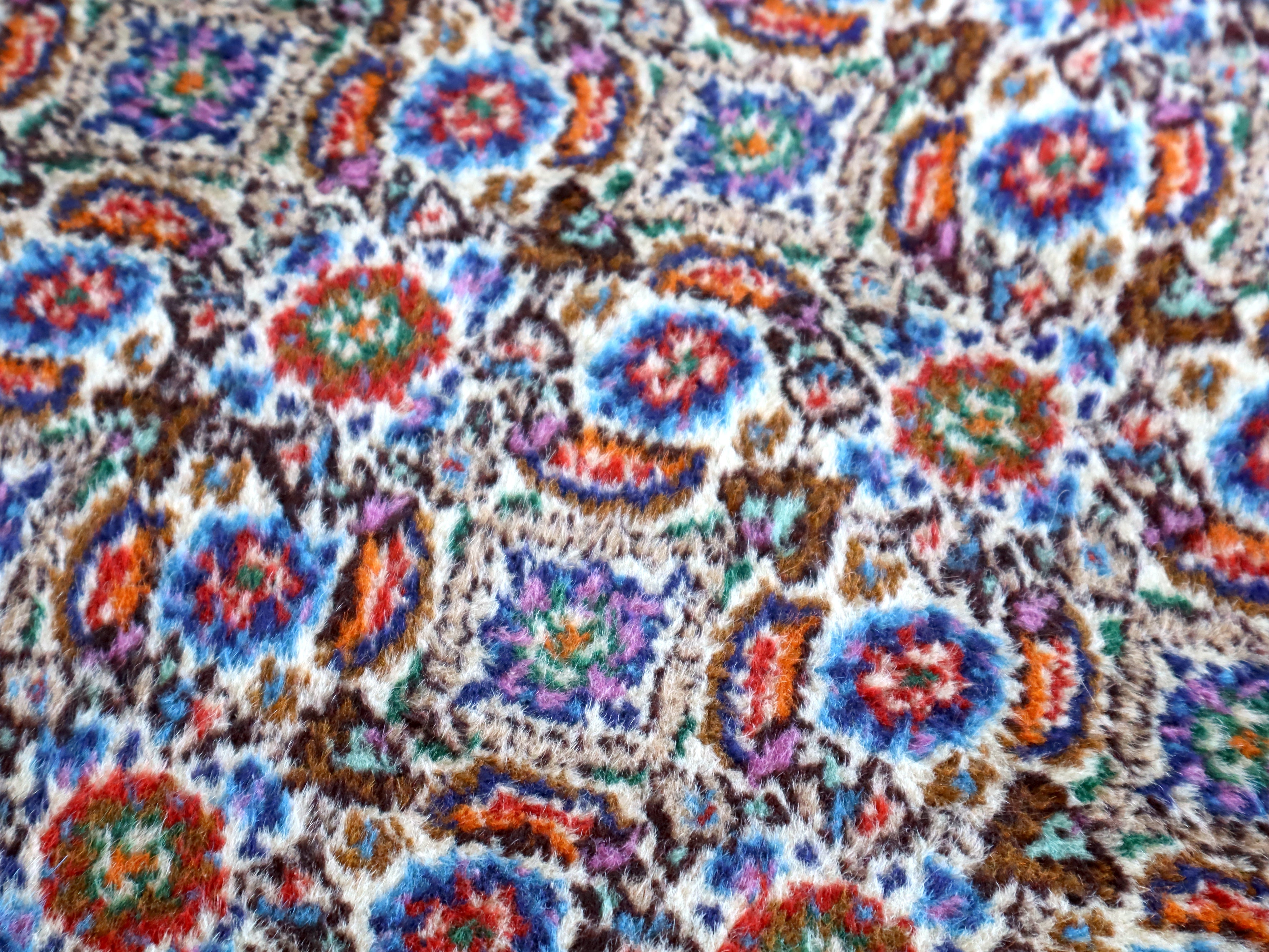 Close-up of rug surface with dense blue, red, and teal floral motifs on light ground