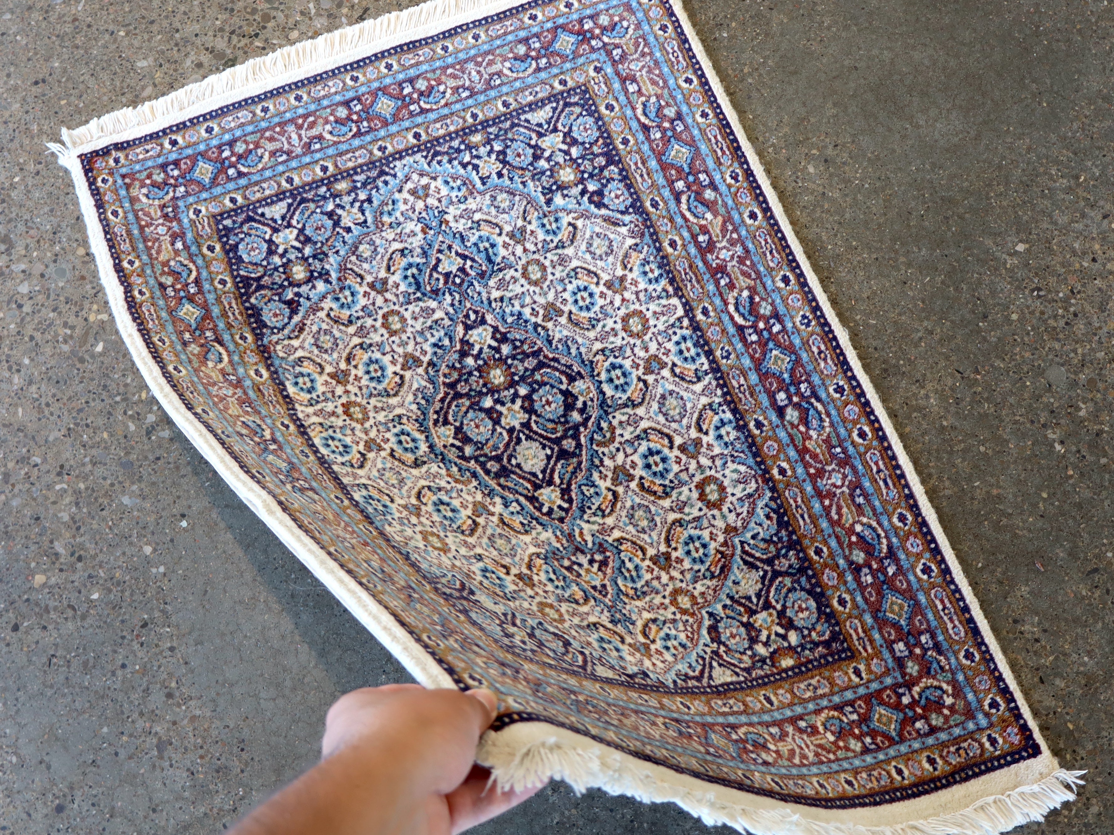 Moud rug shown at an angle with blue and white ornate motif, border trim, and fringe