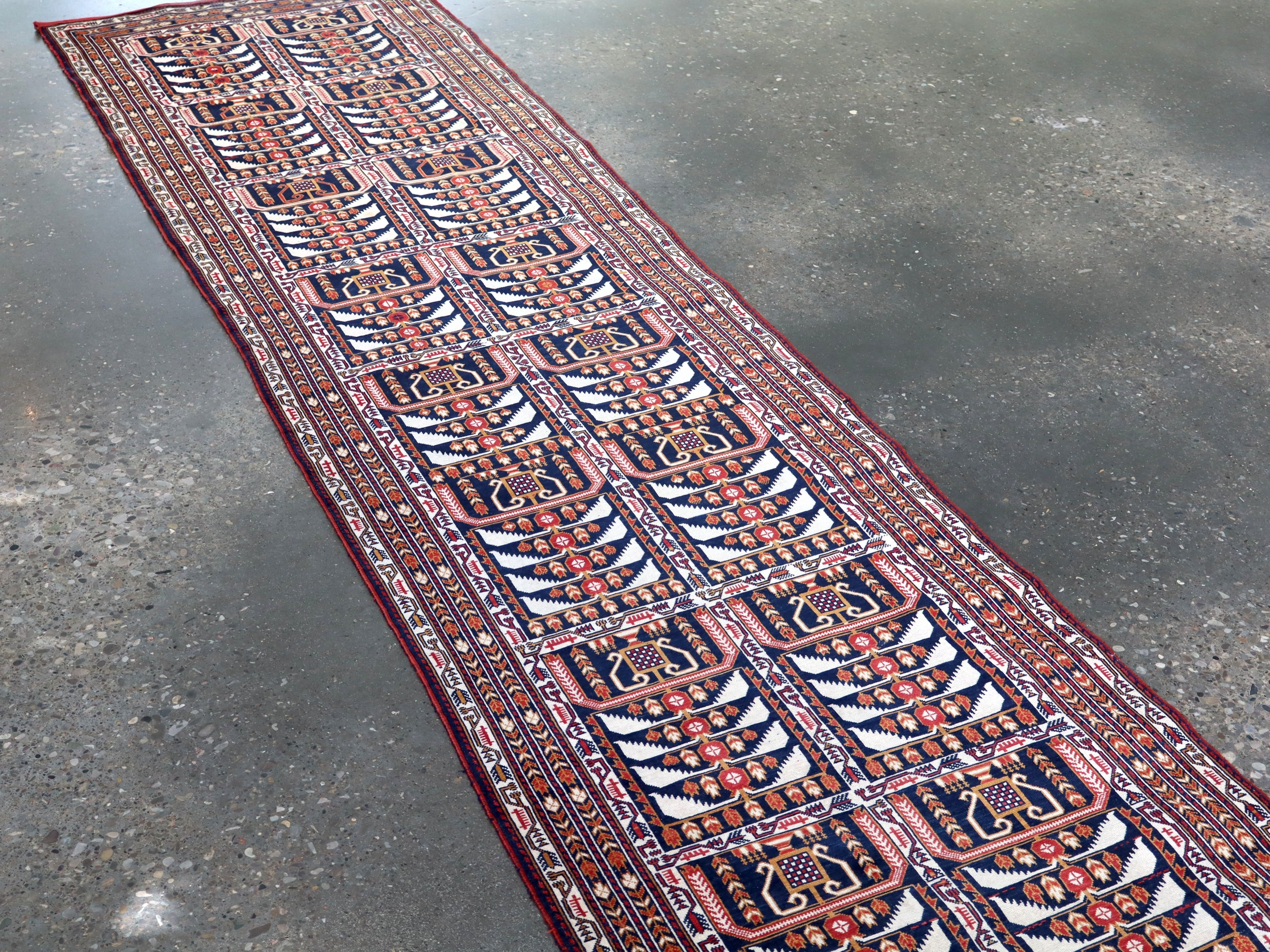 Afghan runner rug angled full view with navy, red, and cream ornamental panels.