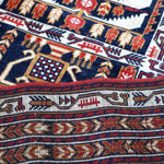 Afghan runner rug close-up of dense navy, red, and cream patterned bands and stars.