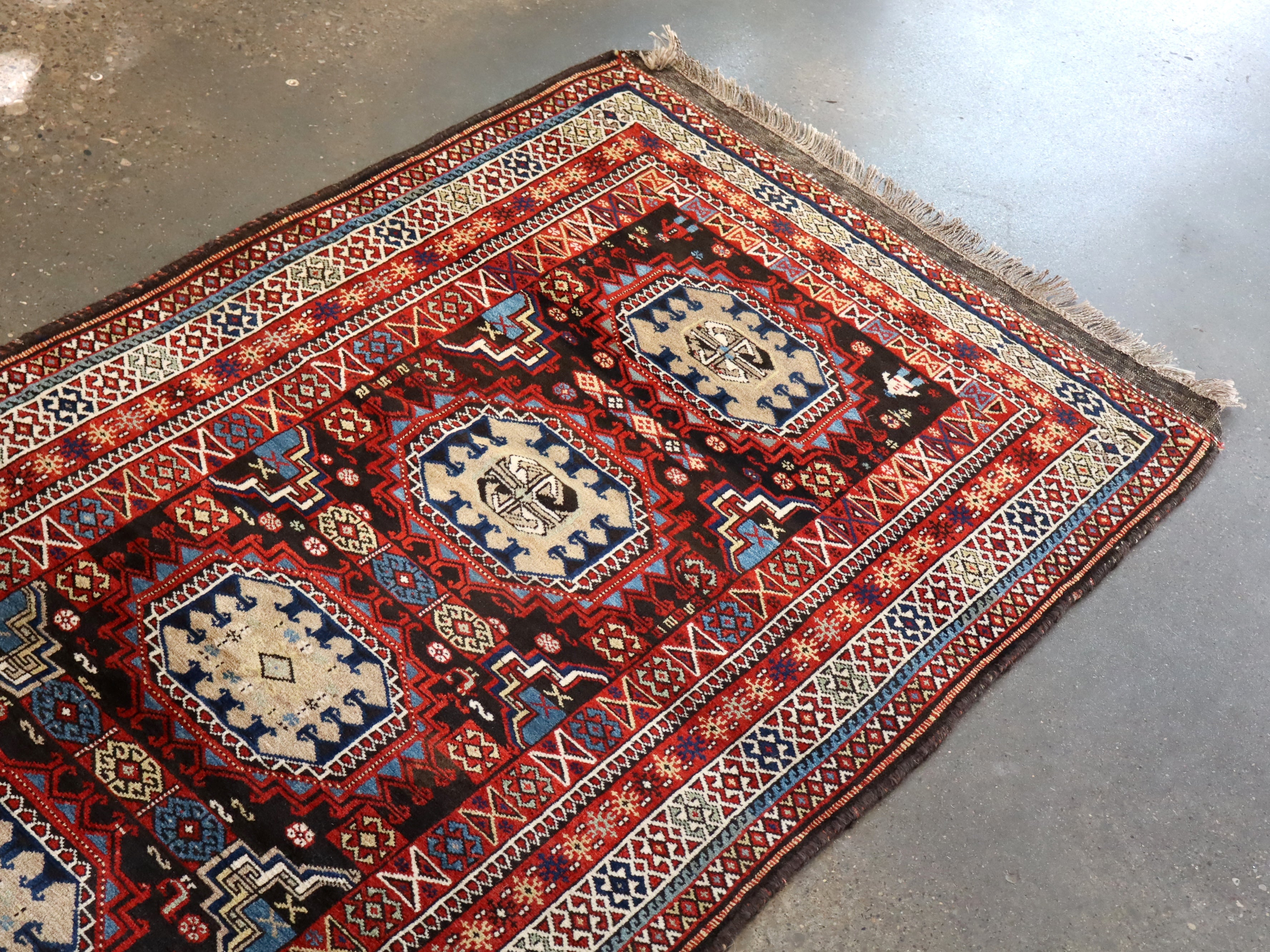 Runner rug flat on concrete floor with red central medallions and blue geometric accents.