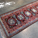 Runner rug wide view with red field, multiple blue medallions, and fringe at ends.