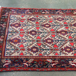 Full rectangular rug with red outer border, dark corner elements, and cream field with blue motifs
