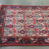 Full rectangular rug with red outer border, dark corner elements, and cream field with blue motifs