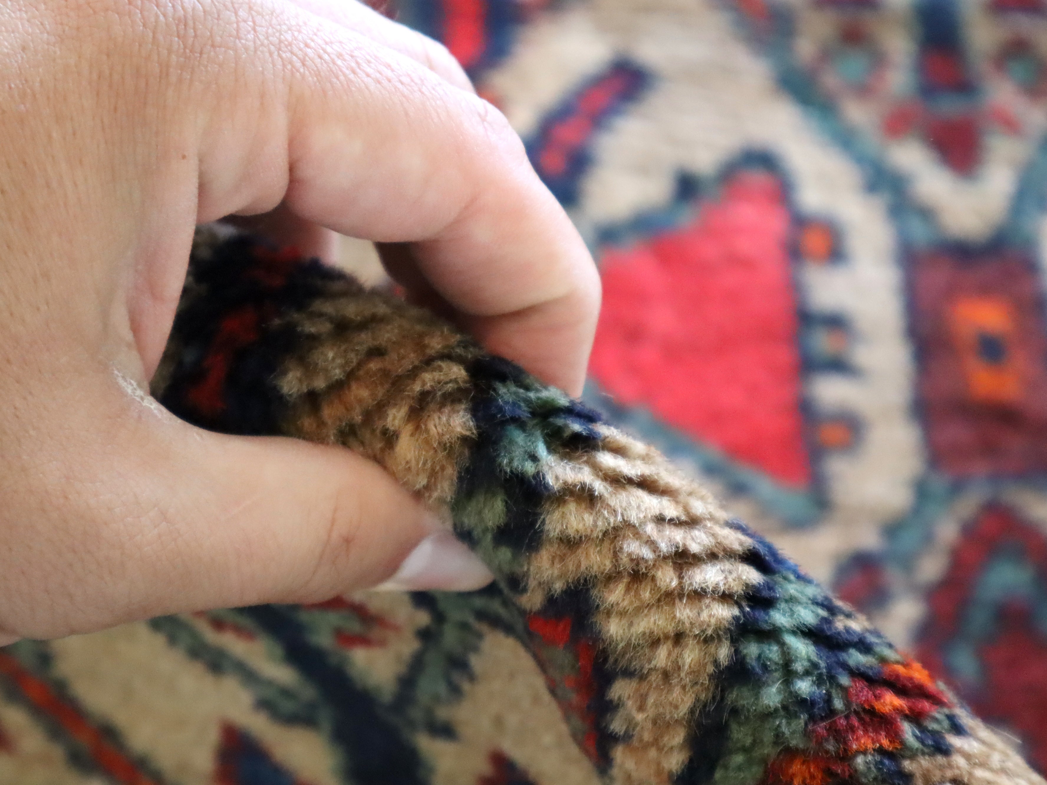 Hand touching rug surface showing dense, textured pile over a blue and red pattern