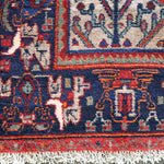 Geometric pattern rug with dark navy border, red accents, and cream fringe edge