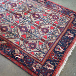 Corner detail of geometric rug with ivory background, red frame, blue medallions, cream fringe