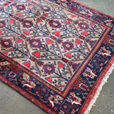Corner detail of geometric rug with ivory background, red frame, blue medallions, cream fringe