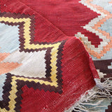 Turkish kilim rug corner with red panel, cream and blue motifs, and fringe
