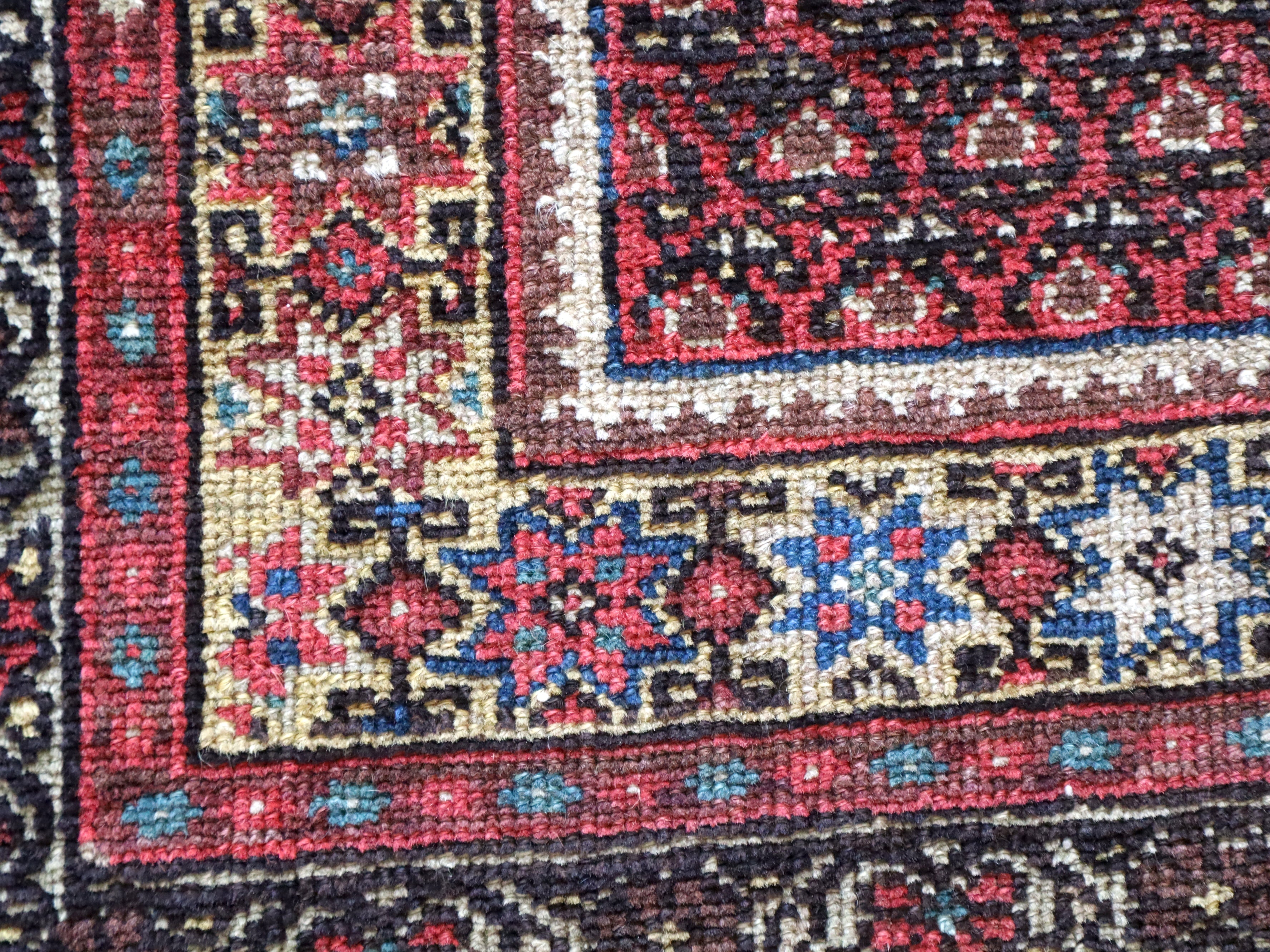 Malayer rug detail with red corner motifs, blue accents, and cream border