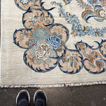 Persian Kashan rug corner detail with layered blue, tan, and gold floral design; fringe