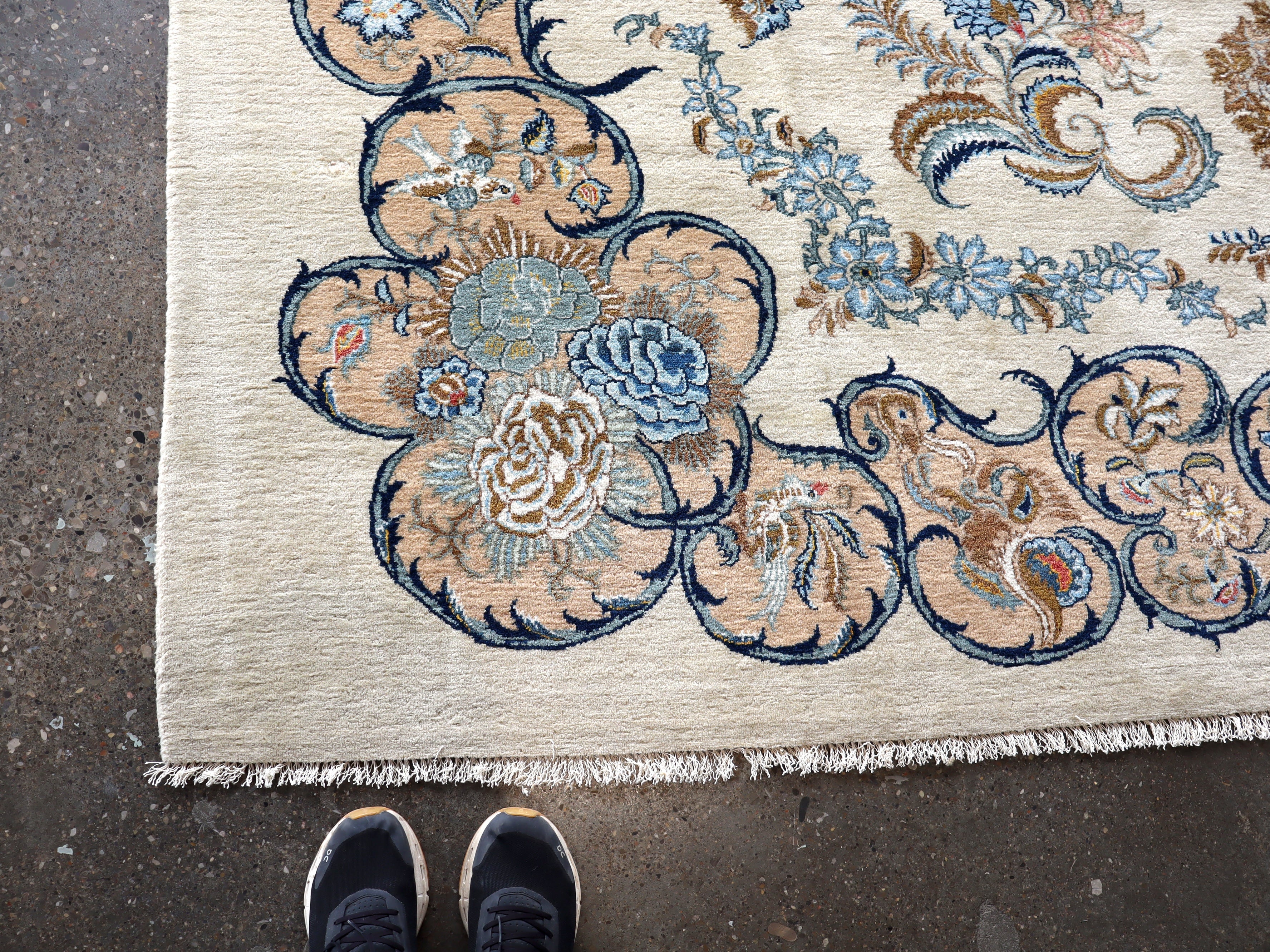 Persian Kashan rug corner detail with layered blue, tan, and gold floral design; fringe