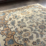 Persian Kashan rug with ivory field and blue floral swirls; decorative corner elements