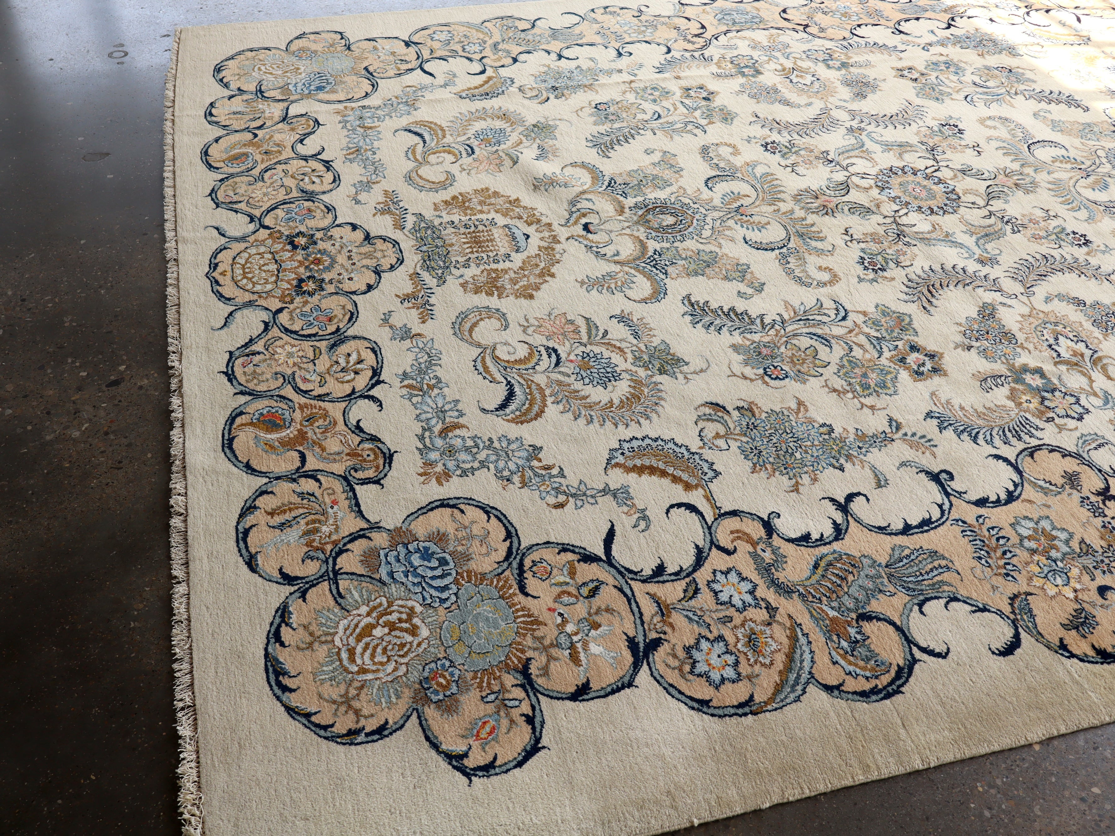 Persian Kashan rug with cream background and dark navy scroll border; floral cluster