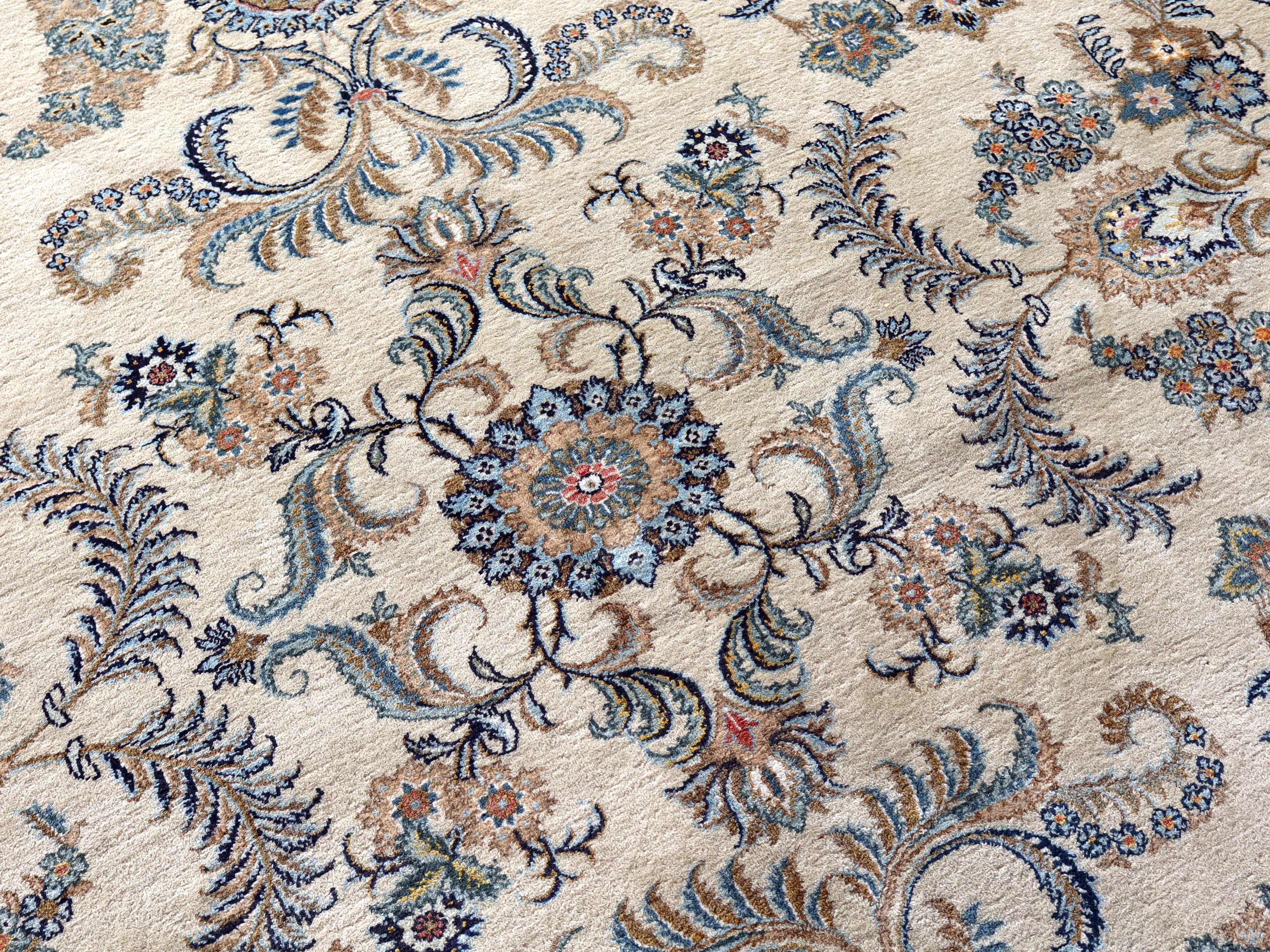 Persian Kashan rug close-up with blue, teal, and tan leaf motifs around a central flower