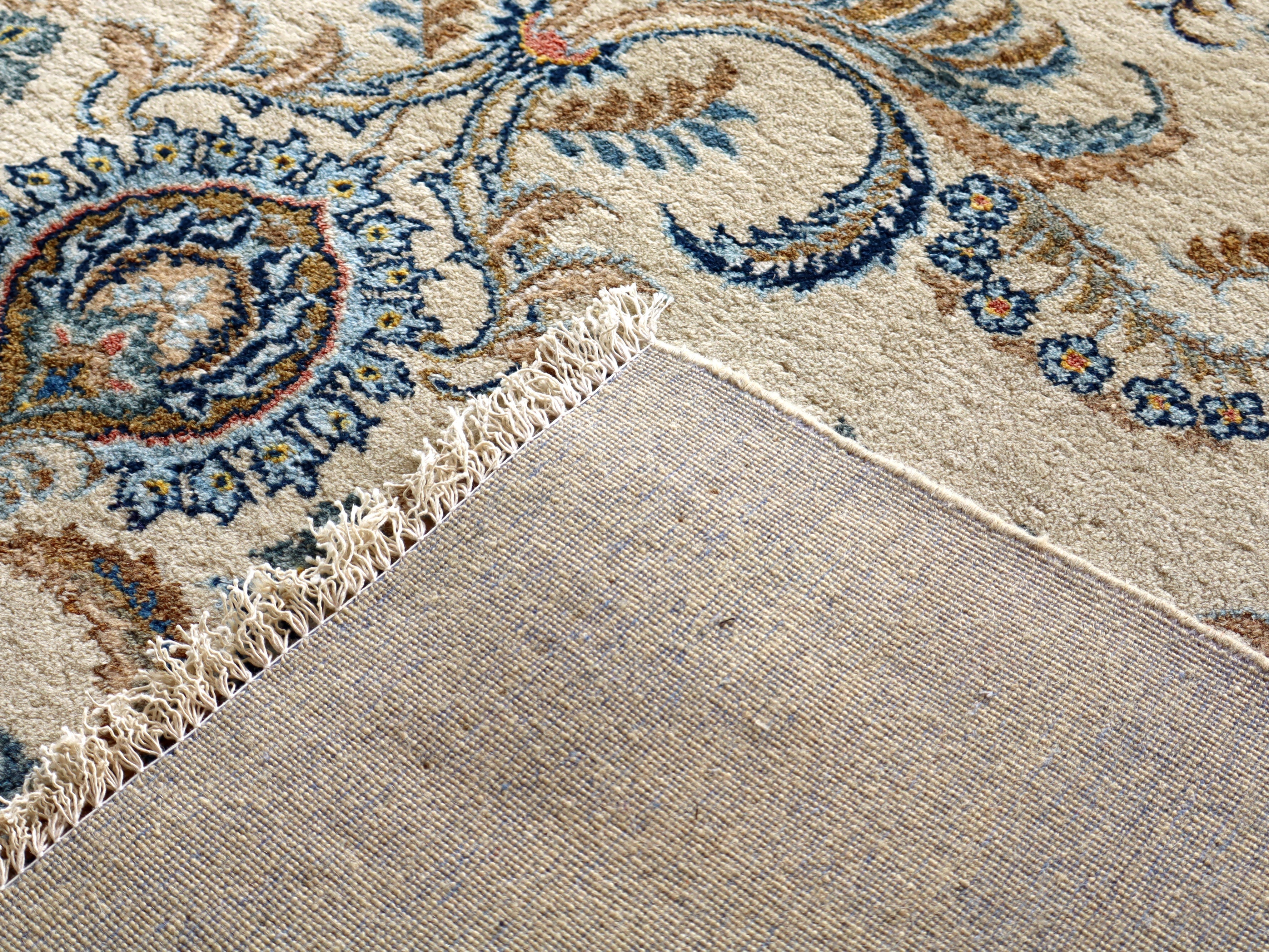 Persian Kashan rug corner with fringed edge and speckled cream pile, blue accents