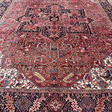 Persian Heriz rug showing large central medallion on red, with ornate geometric bands.