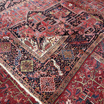 Persian Heriz rug corner detail with red field, navy outlines, cream accents, and fringed edge.