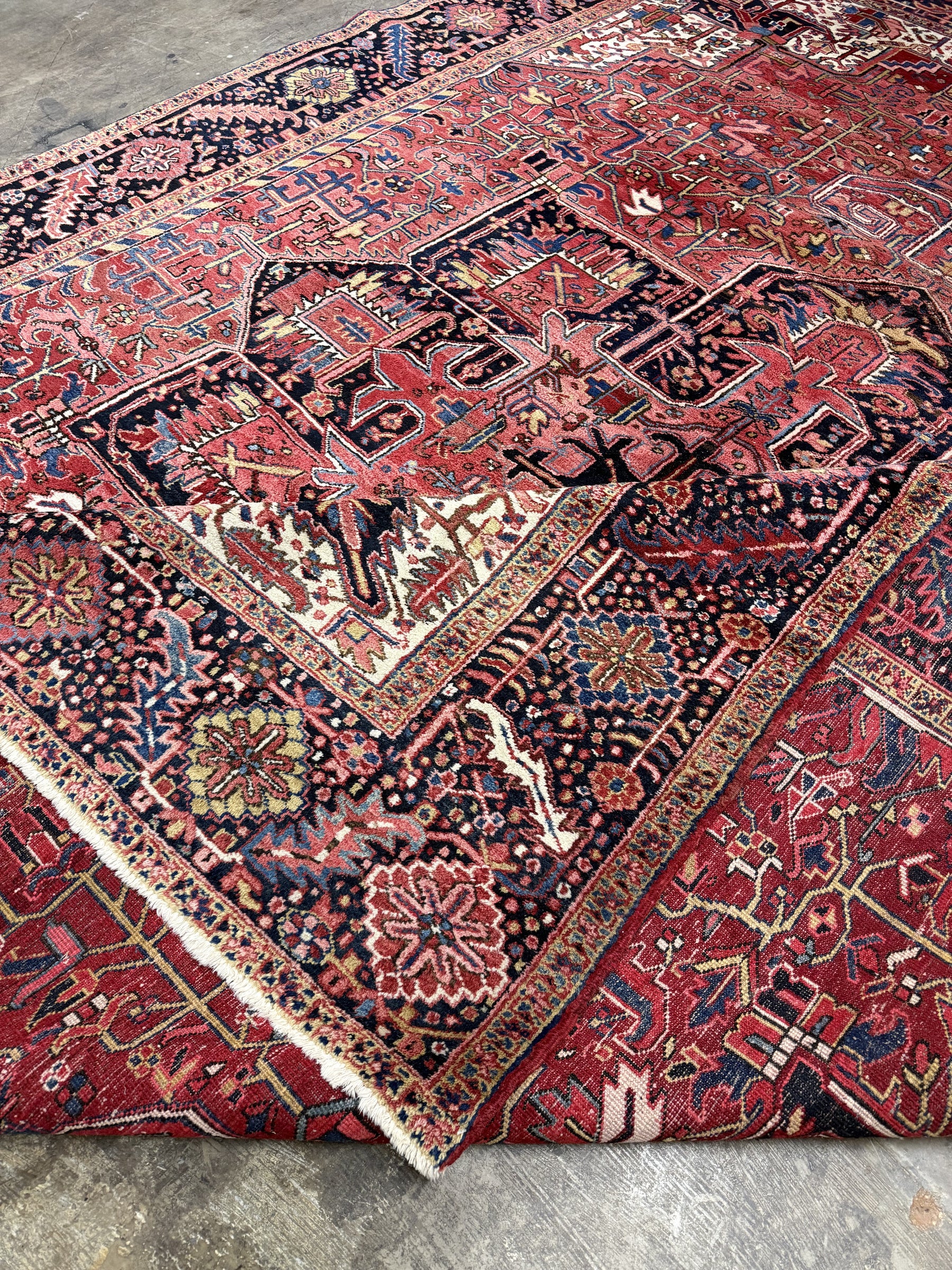 Persian Heriz rug corner detail with red field, navy outlines, cream accents, and fringed edge.