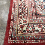 Persian-style rug corner with rust ground, cream field, floral border, and white fringe