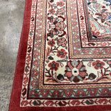 Persian-style rug corner with rust ground, cream field, floral border, and white fringe