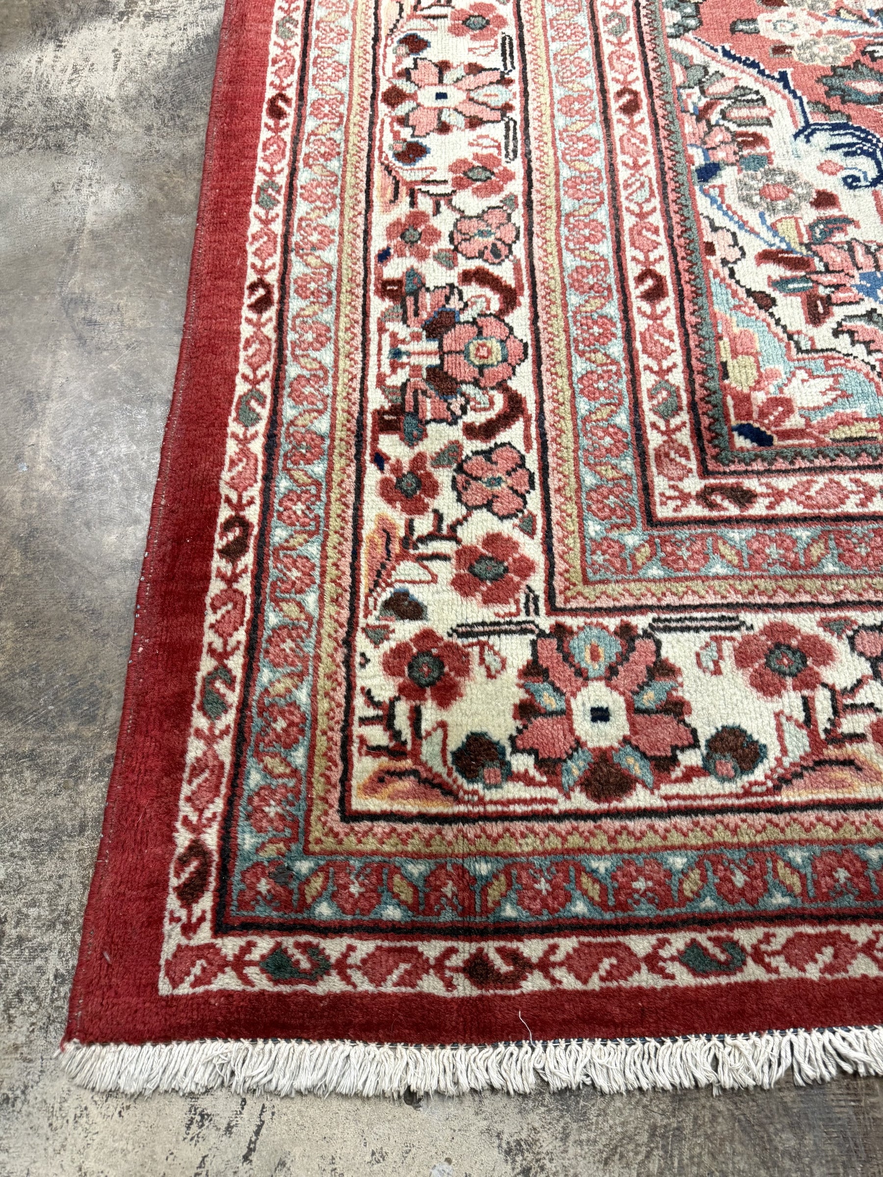 Persian-style rug corner with rust ground, cream field, floral border, and white fringe