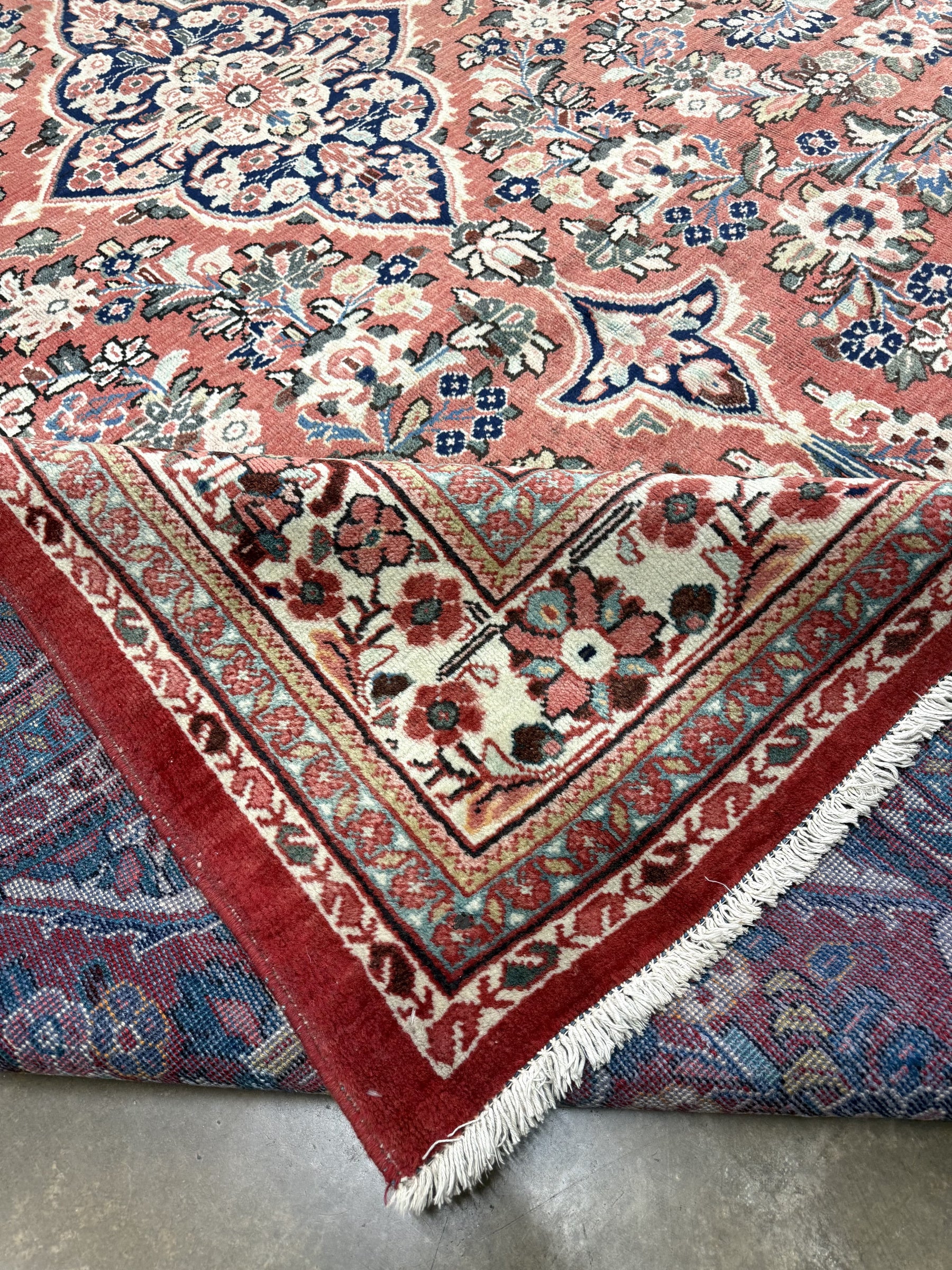 Persian-style rug corner detail with floral border, teal accents, and white fringe edge