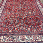 Persian Mahal-style area rug, red field with ornate motifs and cream border fringe.