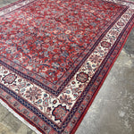Persian Mahal-style area rug with red pattern, navy edging, and cream geometric corner panels.
