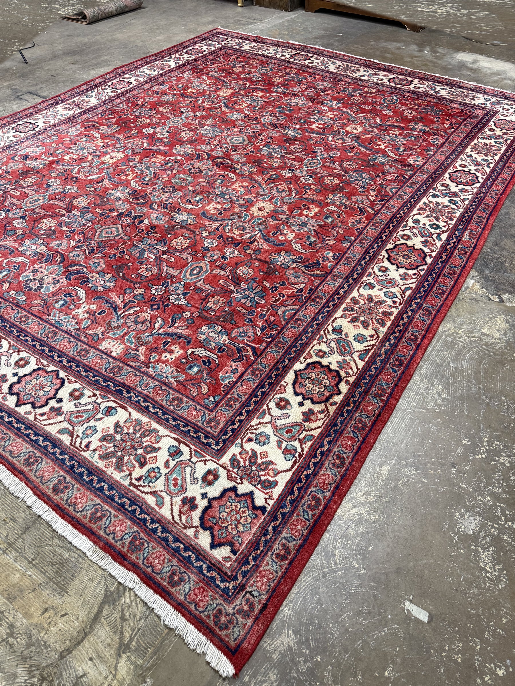 Persian Mahal-style area rug with red pattern, navy edging, and cream geometric corner panels.