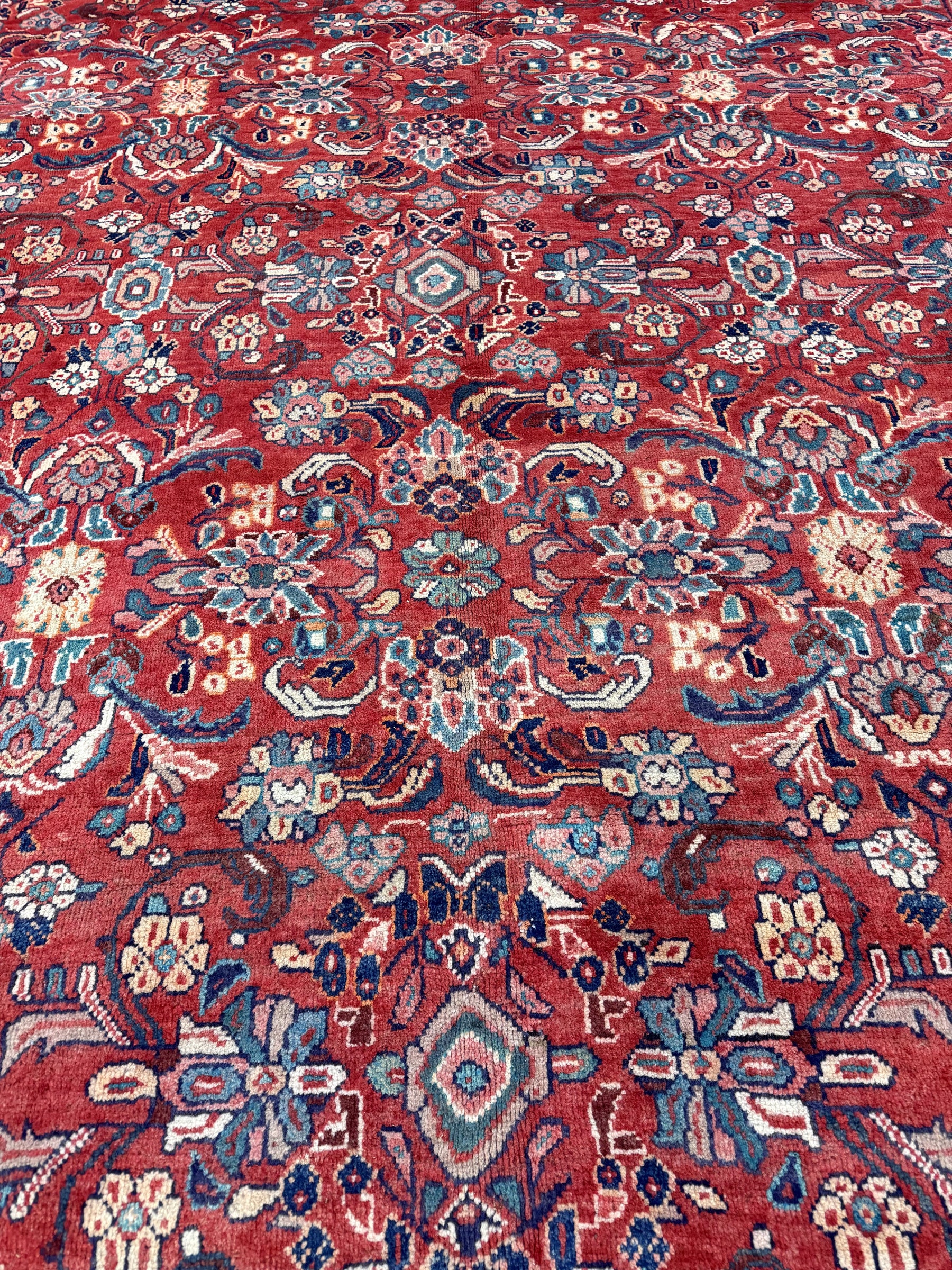 Persian Mahal-style rug close-up with red florals, blue accents, and multicolor medallions.