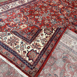 Persian Mahal-style rug corner showing red pattern on top and light backing, navy trim.