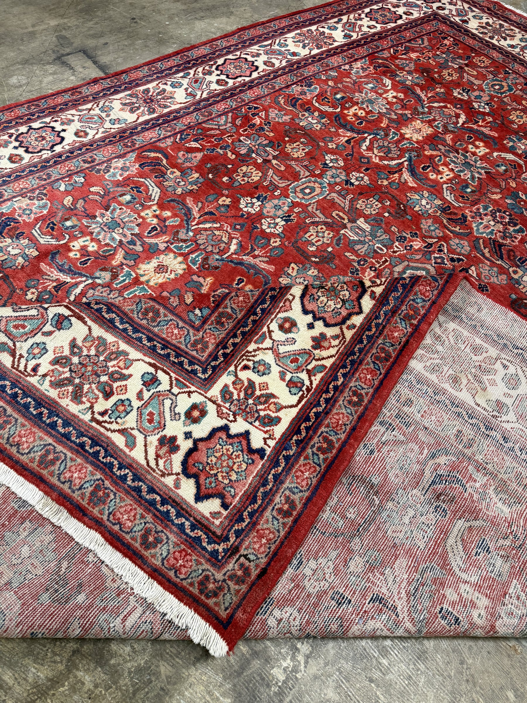Persian Mahal-style rug corner showing red pattern on top and light backing, navy trim.