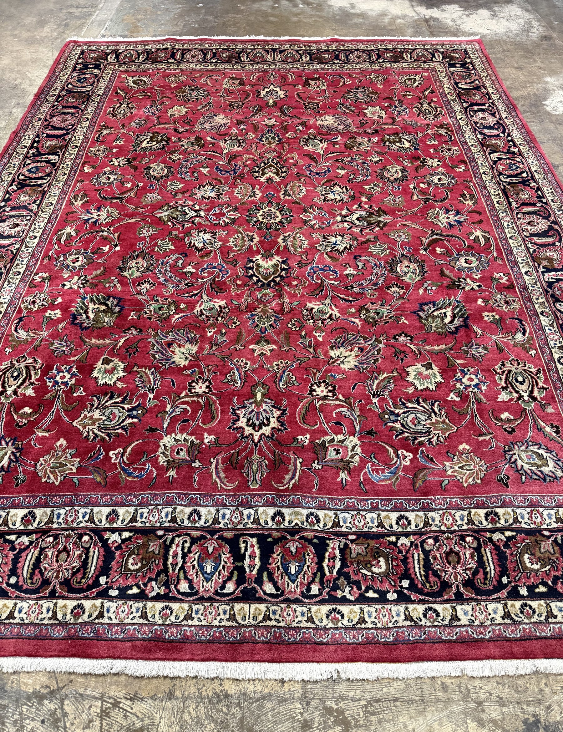 Red Persian-style rug featuring central floral motif, dark blue side border, fringed edge
