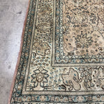 Tabriz-style rug corner, cream with teal-blue border and dense floral designs.